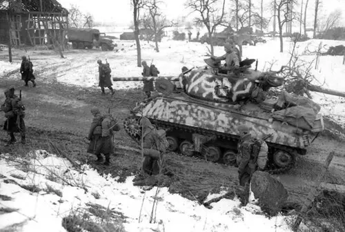 A winter-camouflaged M4A3 76W Sherman tank with a 76mm gun, belonging to the 709th or 750th Tank Battalion, supporting the 75th Infantry Division, driving through the village of Riedwihr (now Porte-du-Ried) in the Colmar region of France, 31 January 1945.